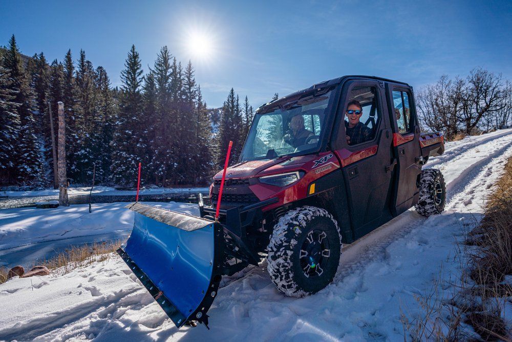 A man is driving a red atv with a snow plow attached to it.