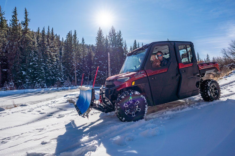 A red pickup truck with a snow plow attached to it is driving down a snow covered road.