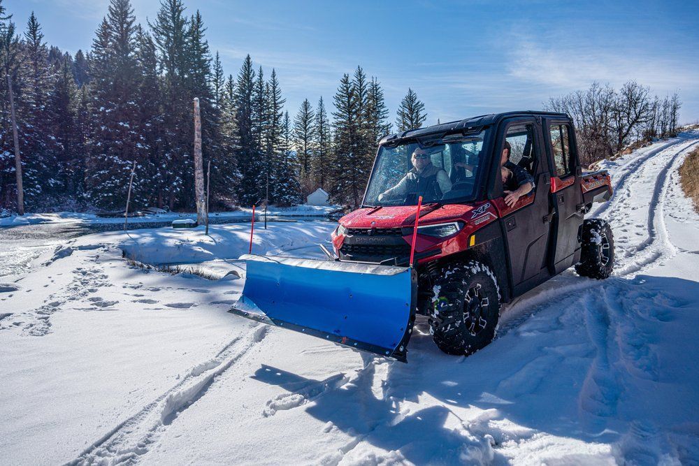 A red utility vehicle with a snow plow attached to it is driving down a snow covered road.