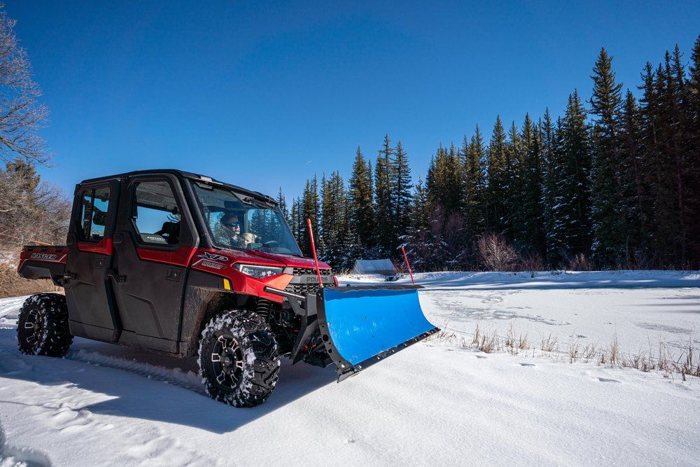 A red atv with a blue plow attached to it is driving through the snow.