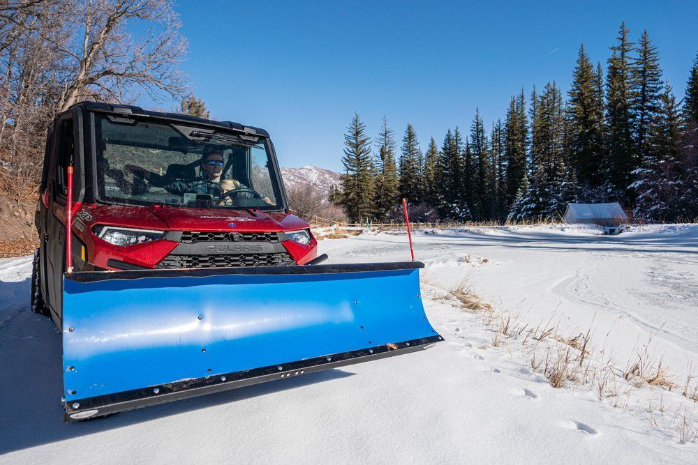 A red vehicle with a blue snow plow is parked in the snow.