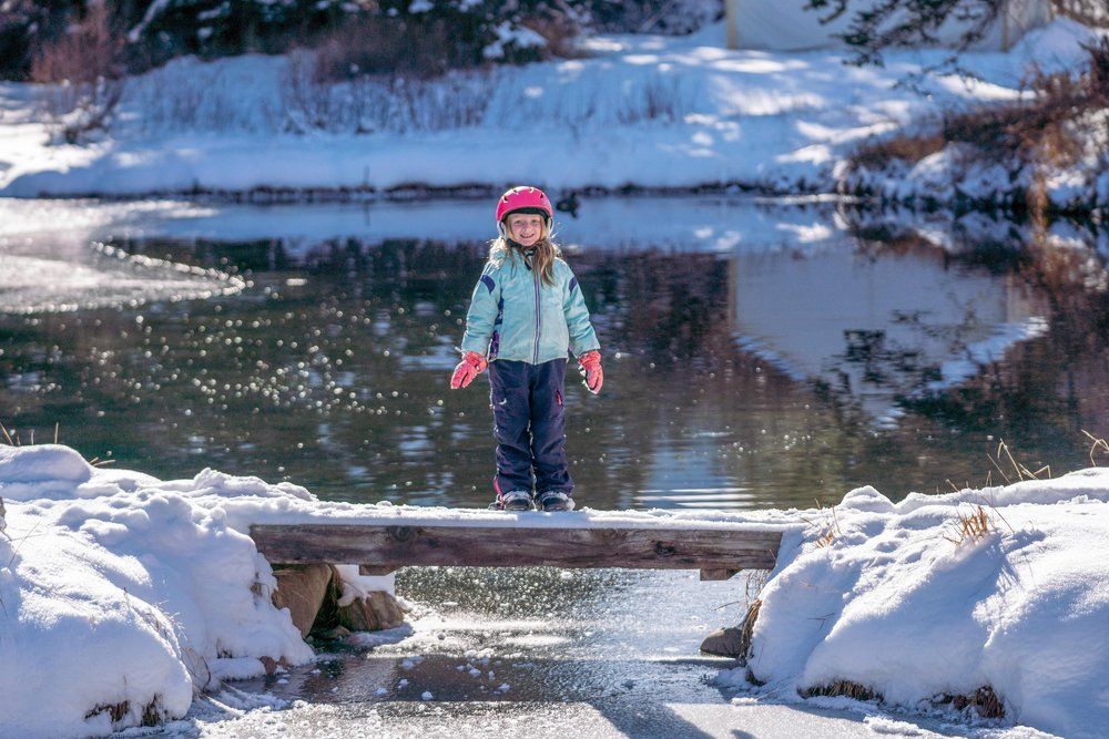 A little girl is standing on a wooden bridge over a river.