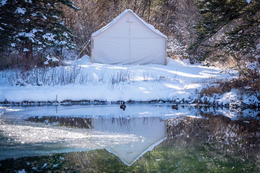 A white tent is sitting on top of a snow covered hill next to a body of water.