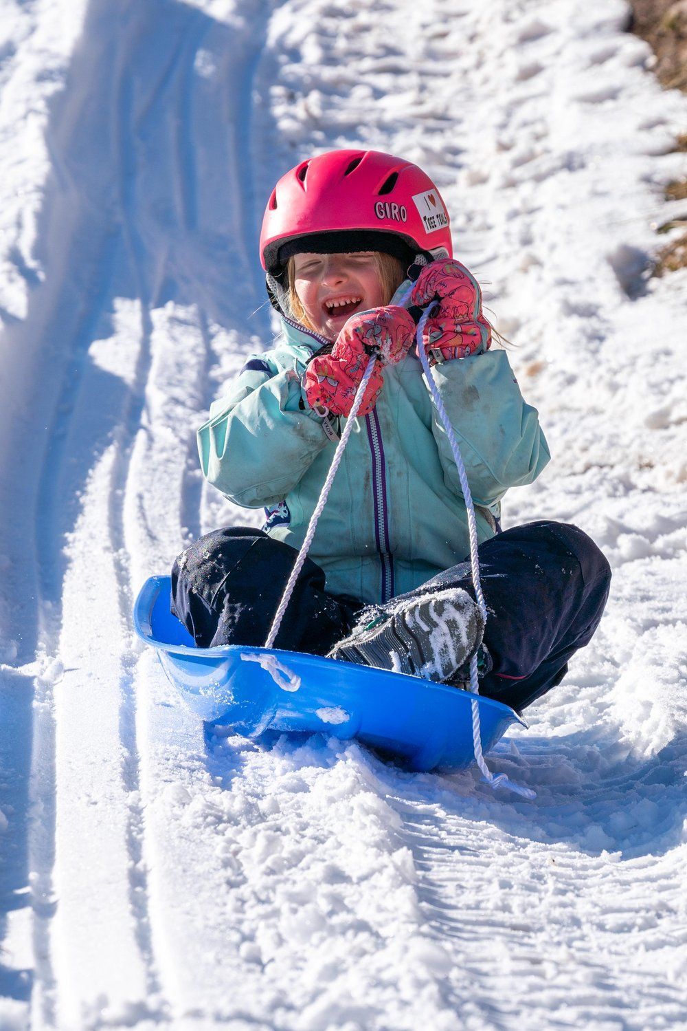 A little girl is sitting on a sled in the snow.