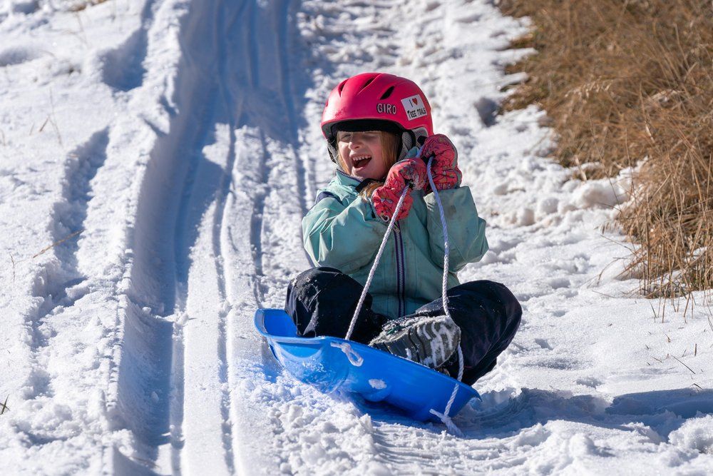 A little girl wearing a pink helmet is sledding down a snowy hill.