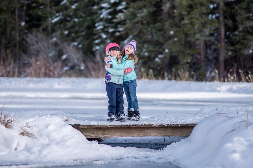 Two children are standing on a bridge in the snow.