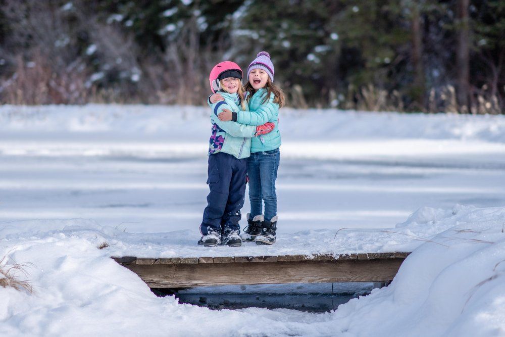 Two little girls are standing on a bridge in the snow.
