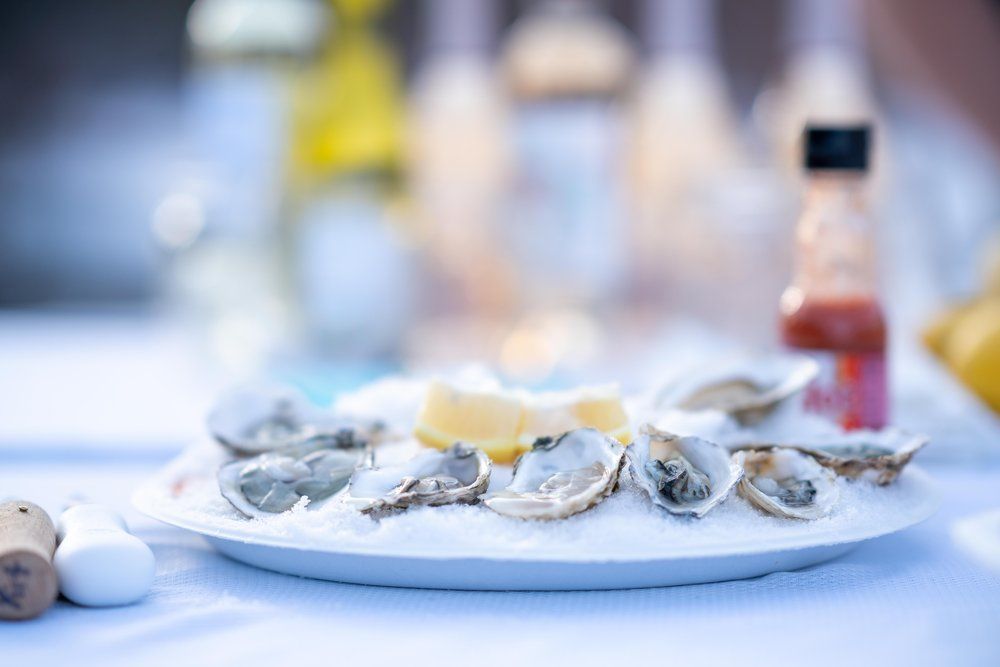 A plate of oysters on ice with a lemon wedge on a table.