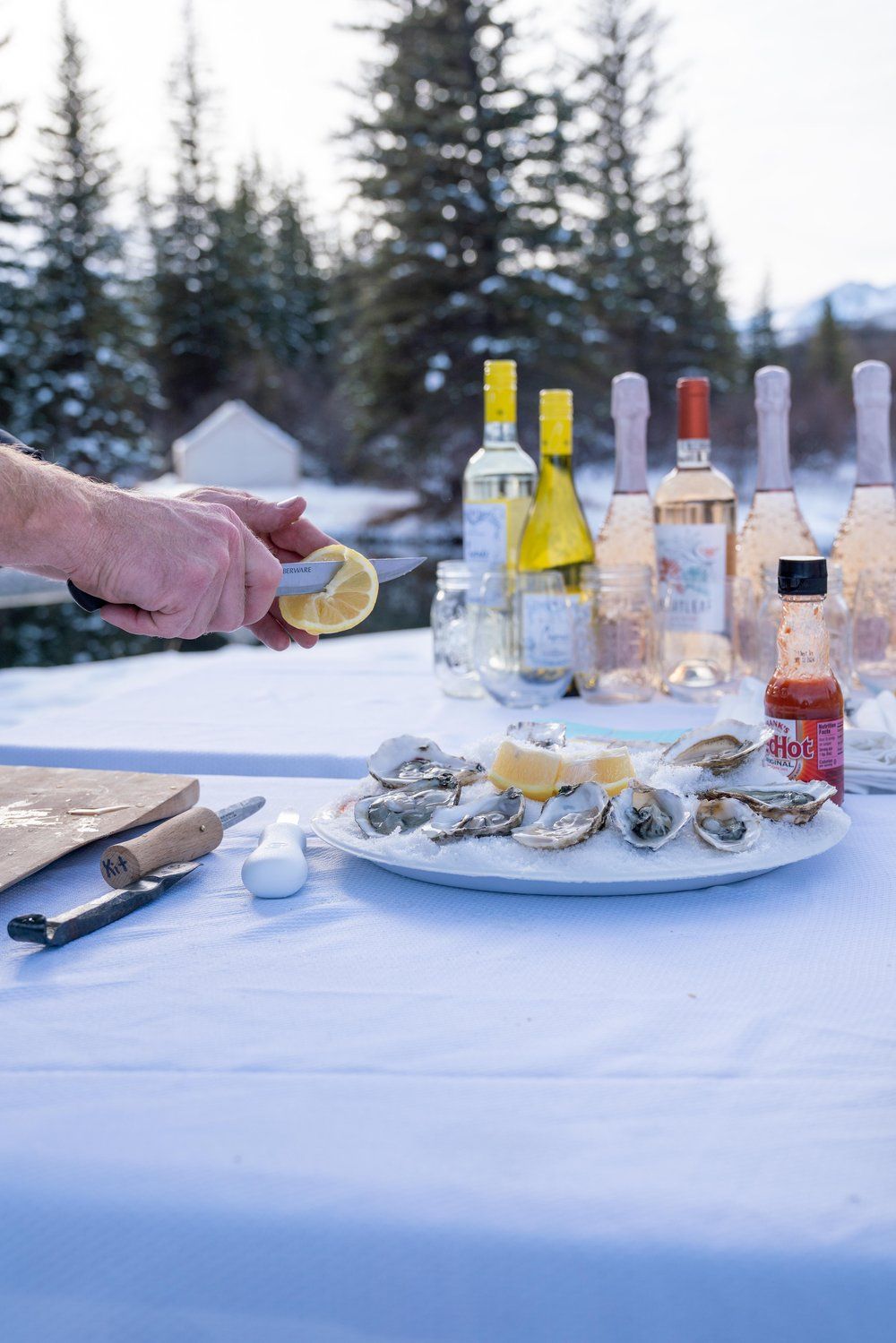 A person is squeezing a lemon over a plate of oysters on a table.