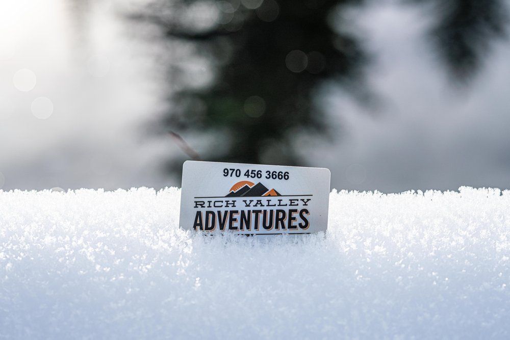 A sign for rich valley adventures is sitting in the snow.