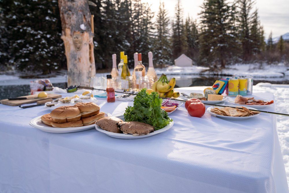A table topped with plates of food and drinks in the snow.