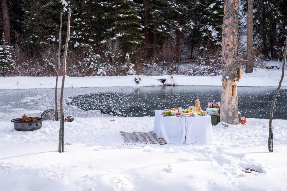 A table is sitting in the snow next to a lake.
