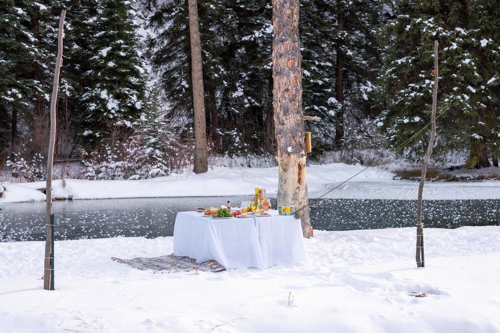 A table with food on it is sitting in the snow near a lake.