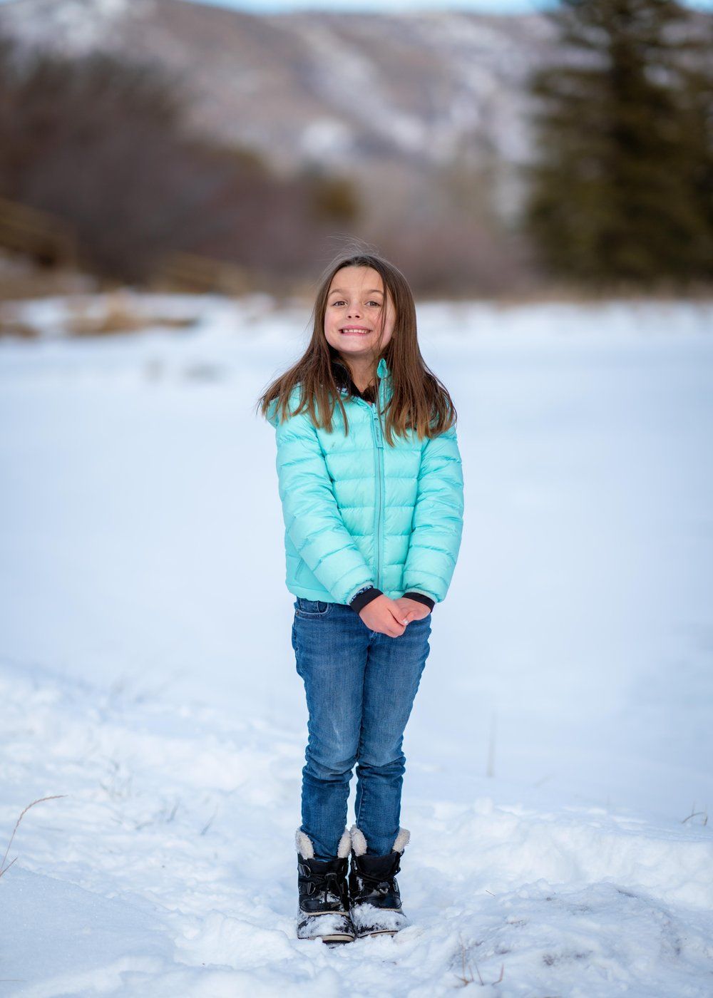 A young girl in a blue jacket and jeans is standing in the snow.