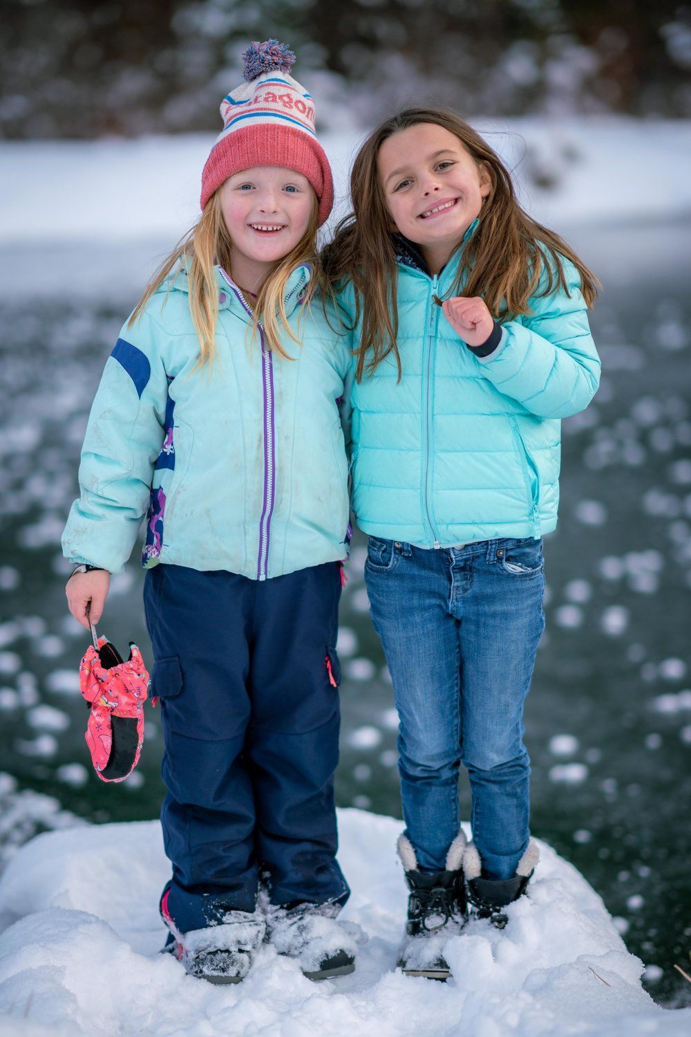 Two little girls are standing next to each other in the snow.