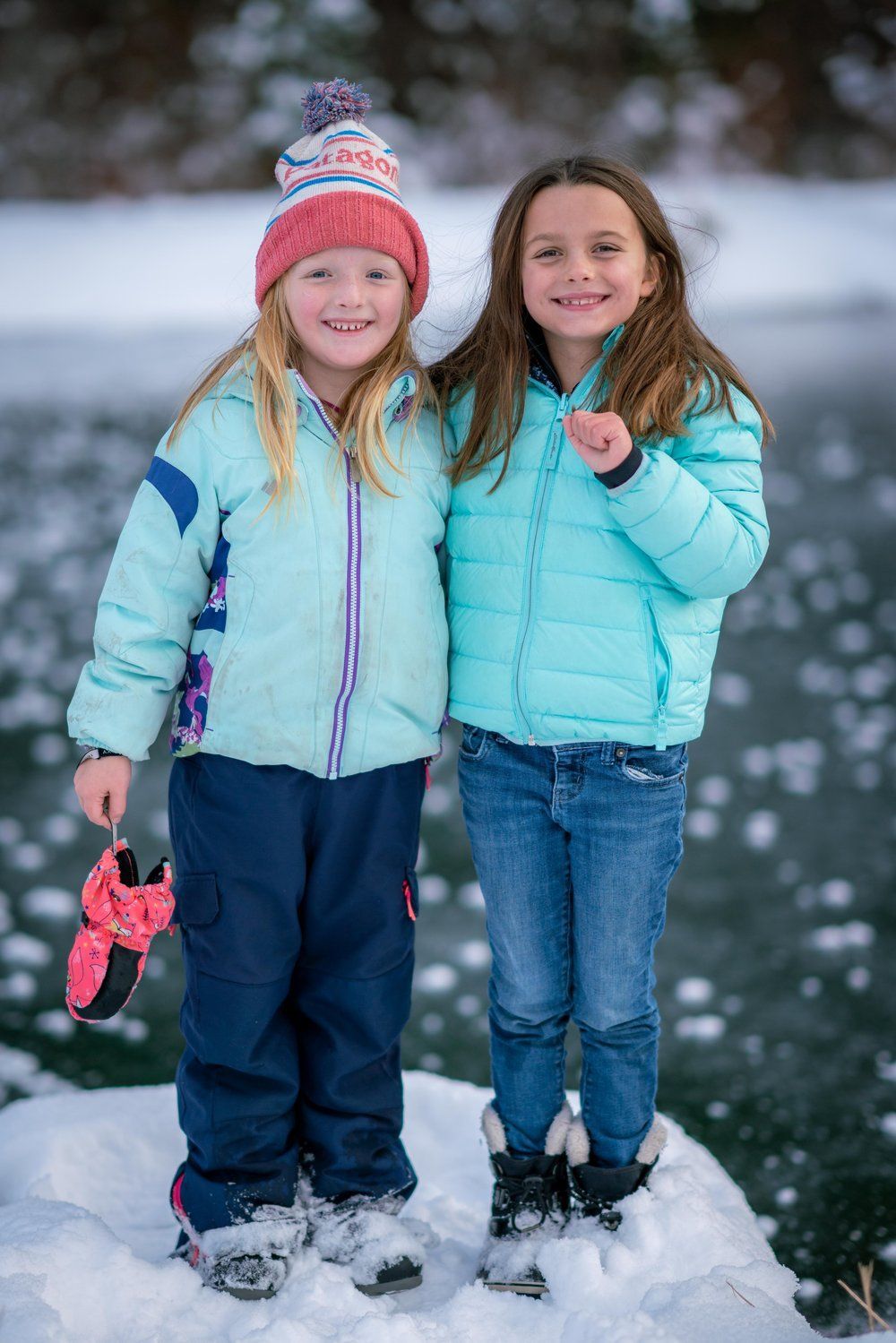 Two young girls are standing next to each other in the snow.