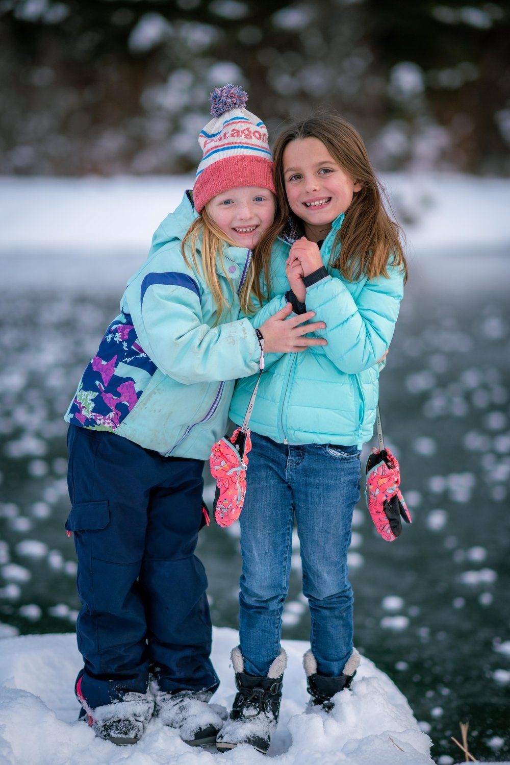 Two little girls are hugging each other in the snow.