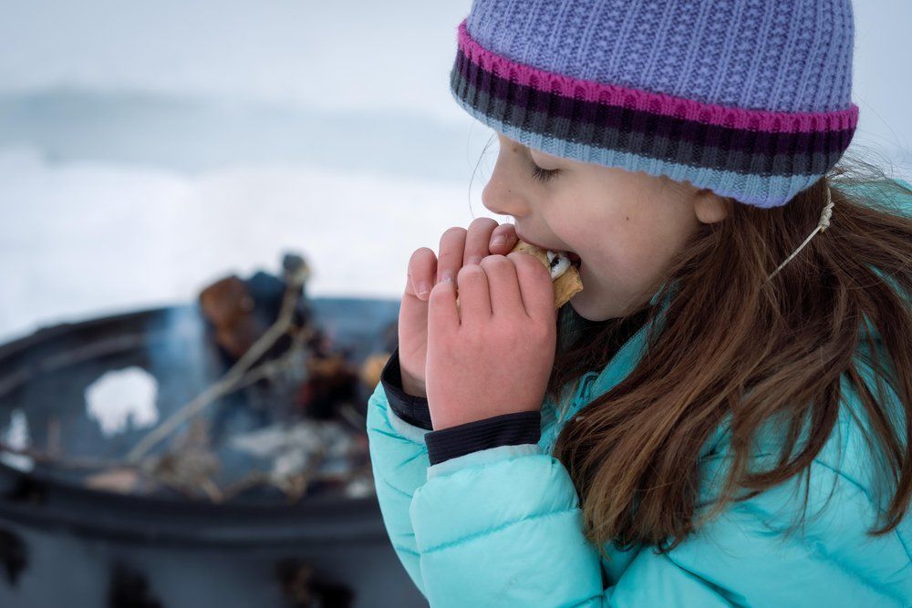 A little girl is eating a s'more in the snow.