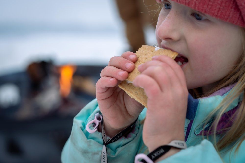 A little girl is eating a s'more in front of a fire.