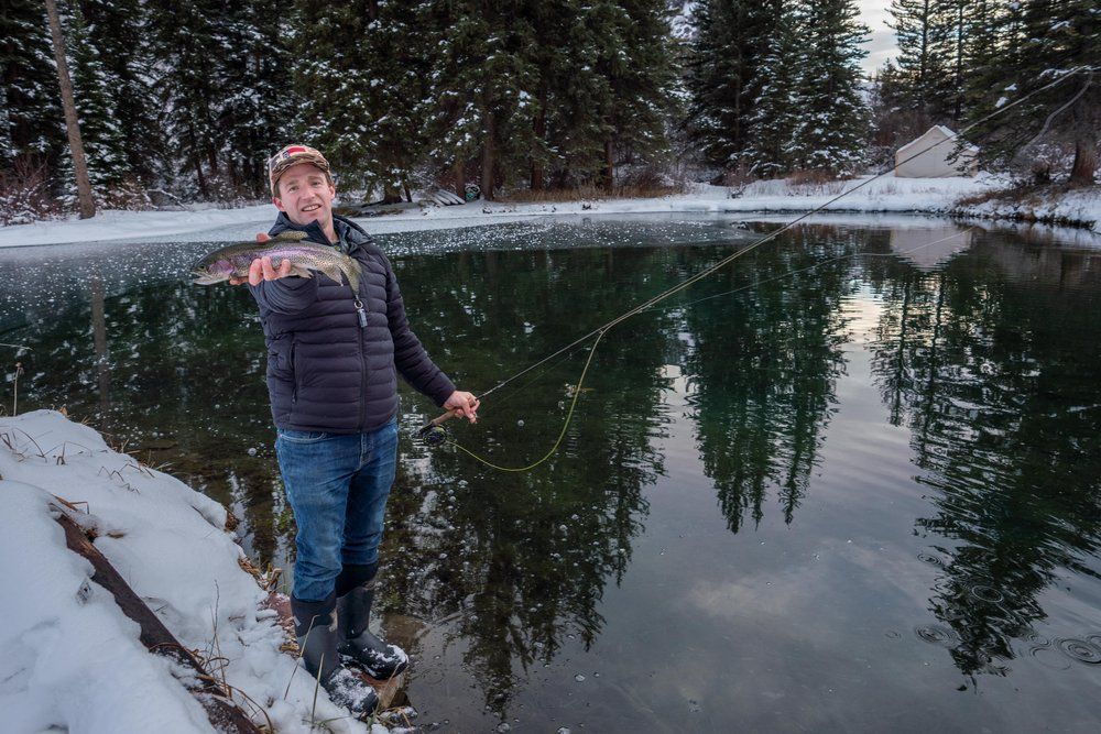 A man is fishing in a lake in the snow.