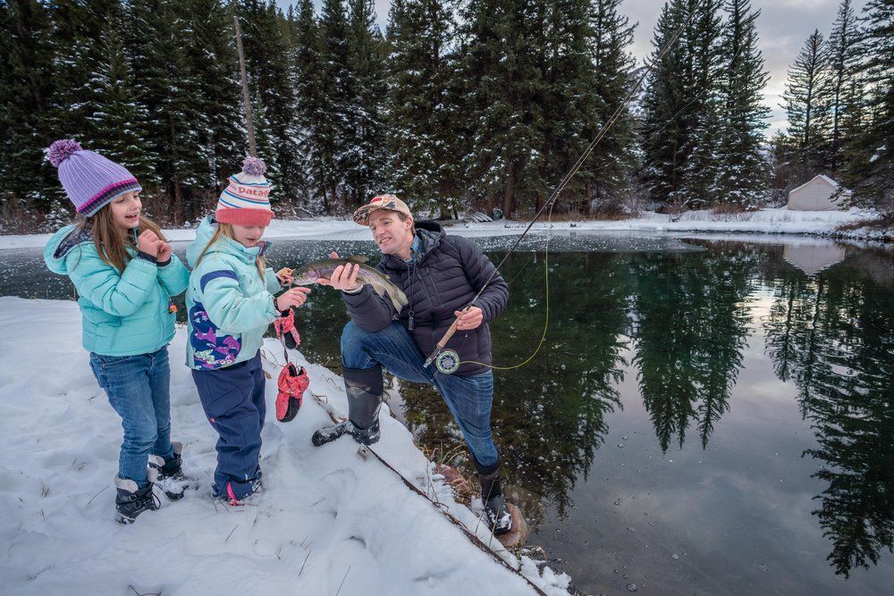 A man and two children are fishing in the snow near a lake.