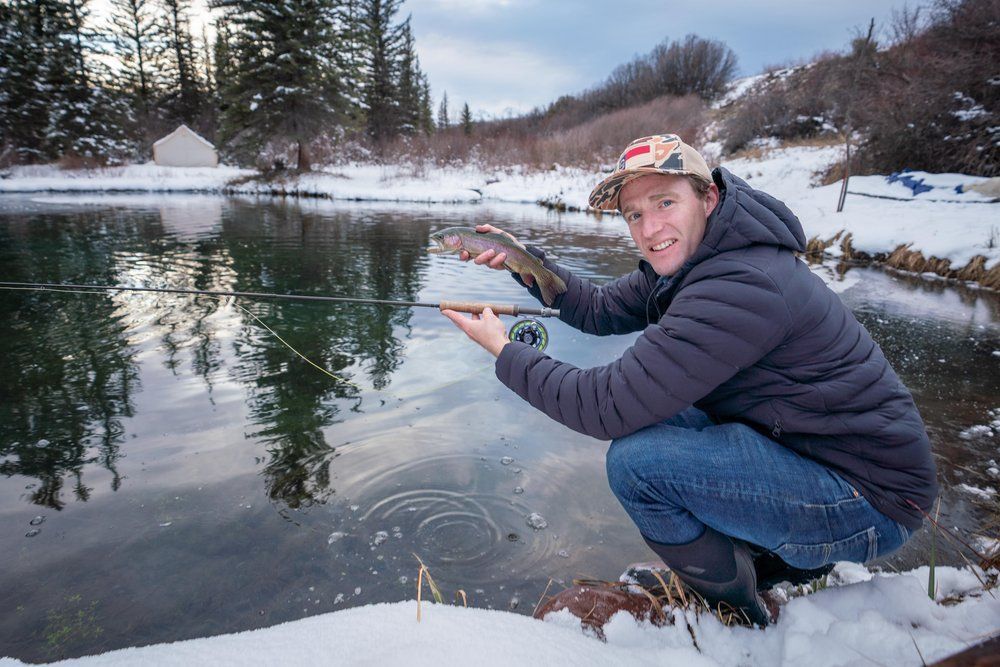 A man is kneeling in the snow holding a fishing rod and a fish.