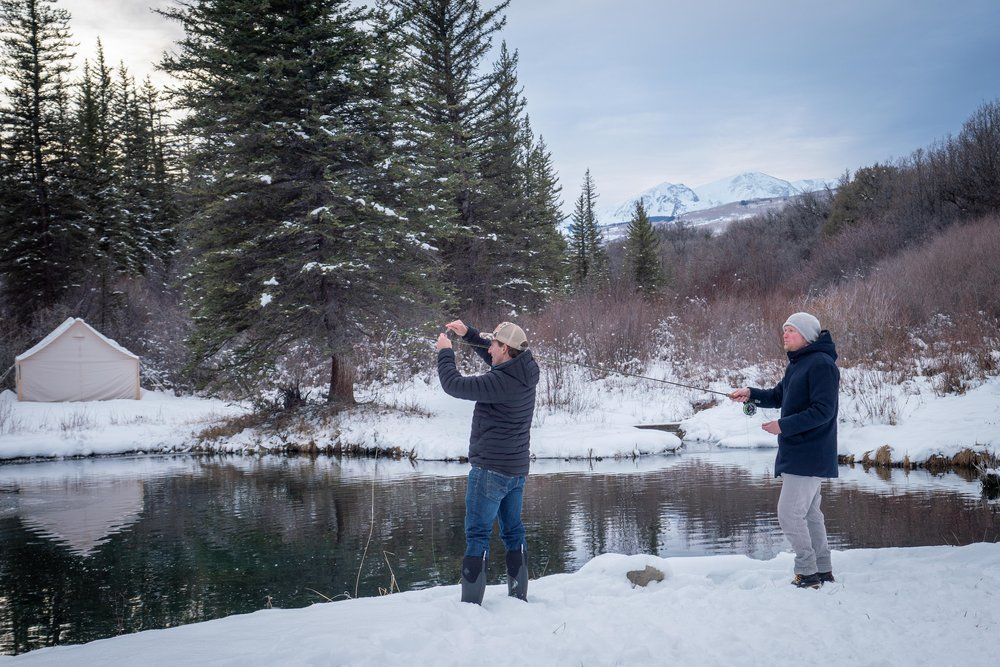 Two men are standing in the snow near a lake taking pictures.