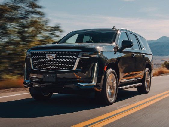 A black suv is driving down a road with mountains in the background.