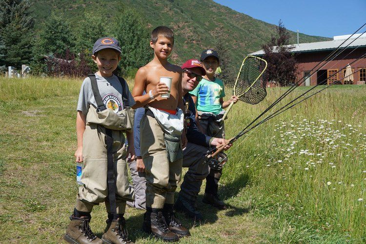 A group of young boys are fishing with a man in a field.