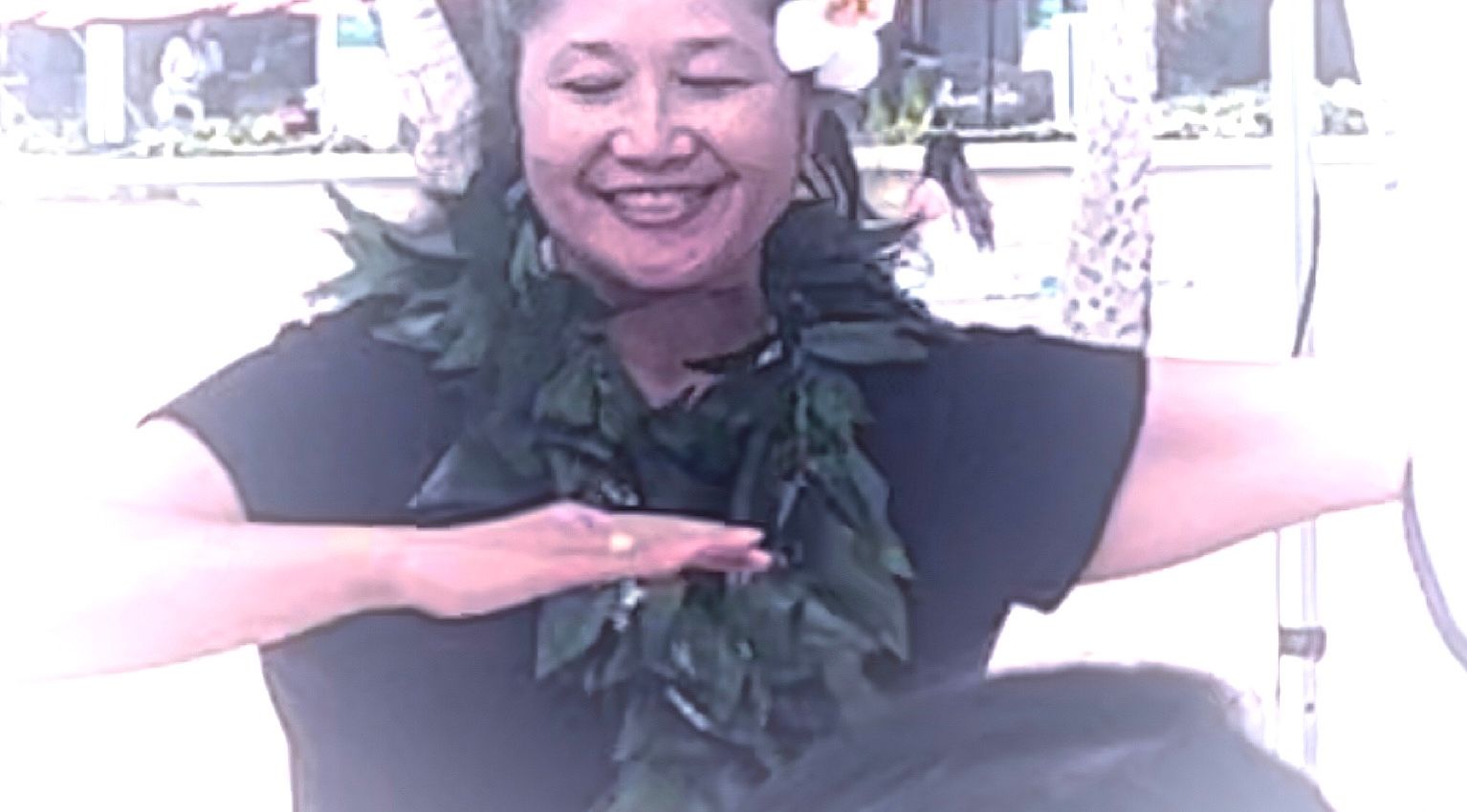 A woman is wearing a lei and smiling while dancing.