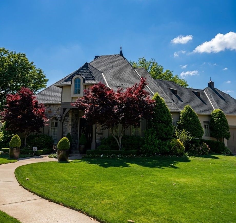 Luxury suburban house with manicured lawn, curved walkway, and trees under a blue sky