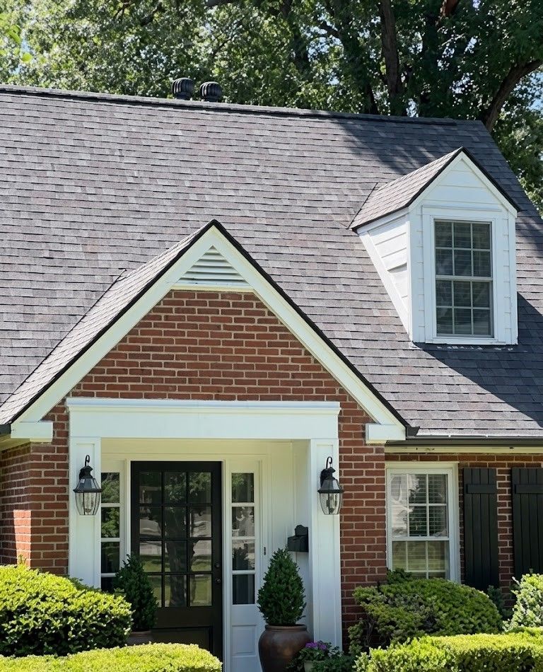 Brick house entrance with white trim, black double doors, and a gabled roof with dormer window.