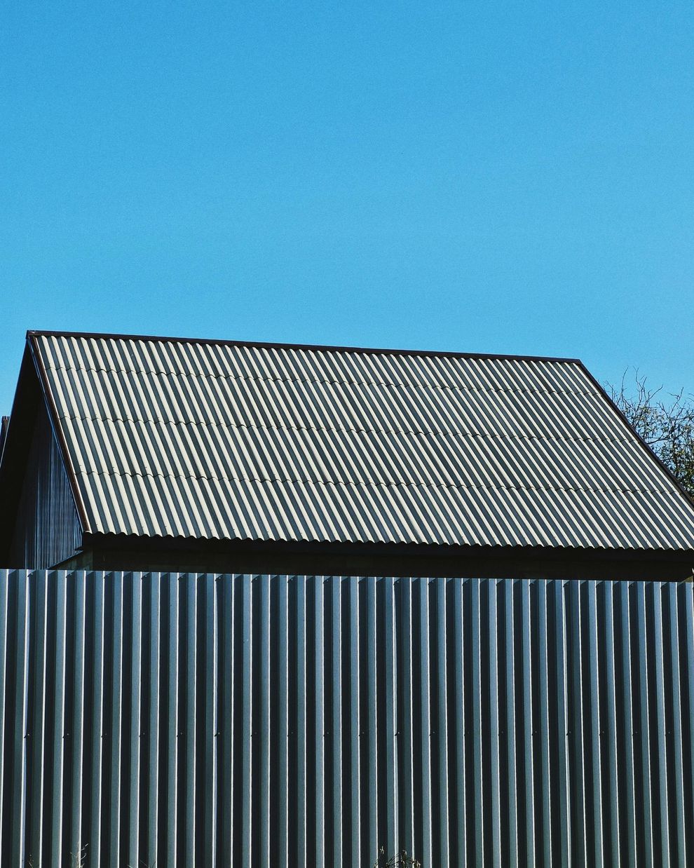 Small house with a corrugated metal roof and wall against a clear blue sky.