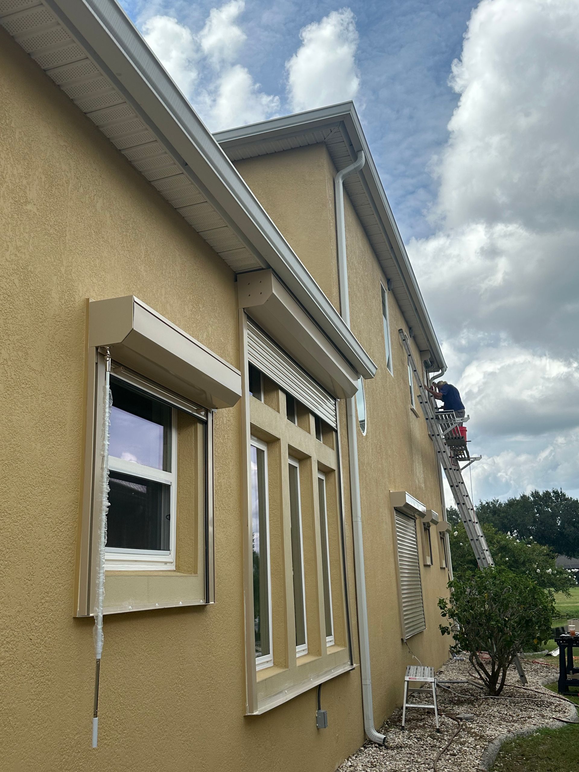 A man on a ladder is painting the side of a house.