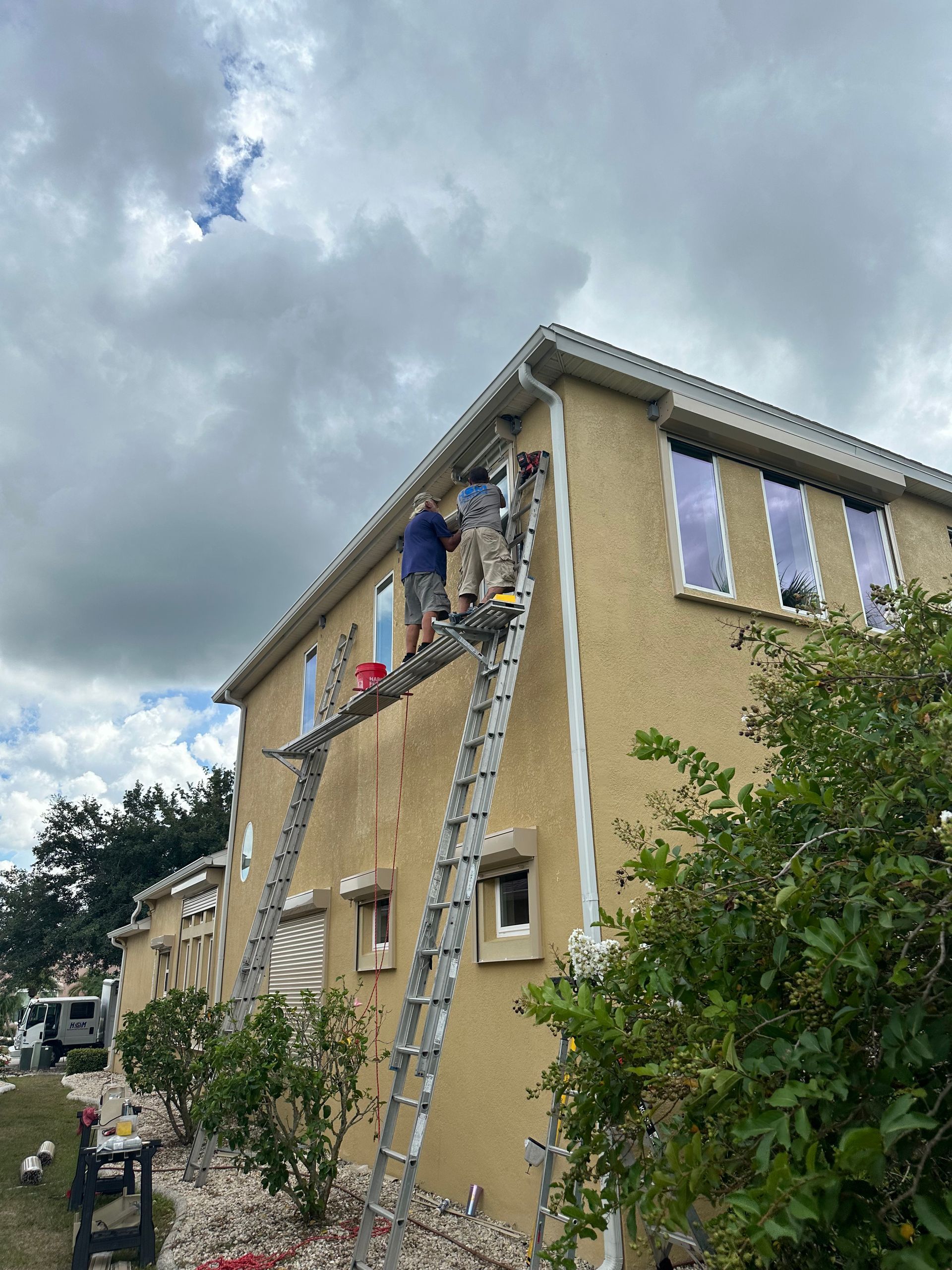 A man on a ladder is painting the side of a house.