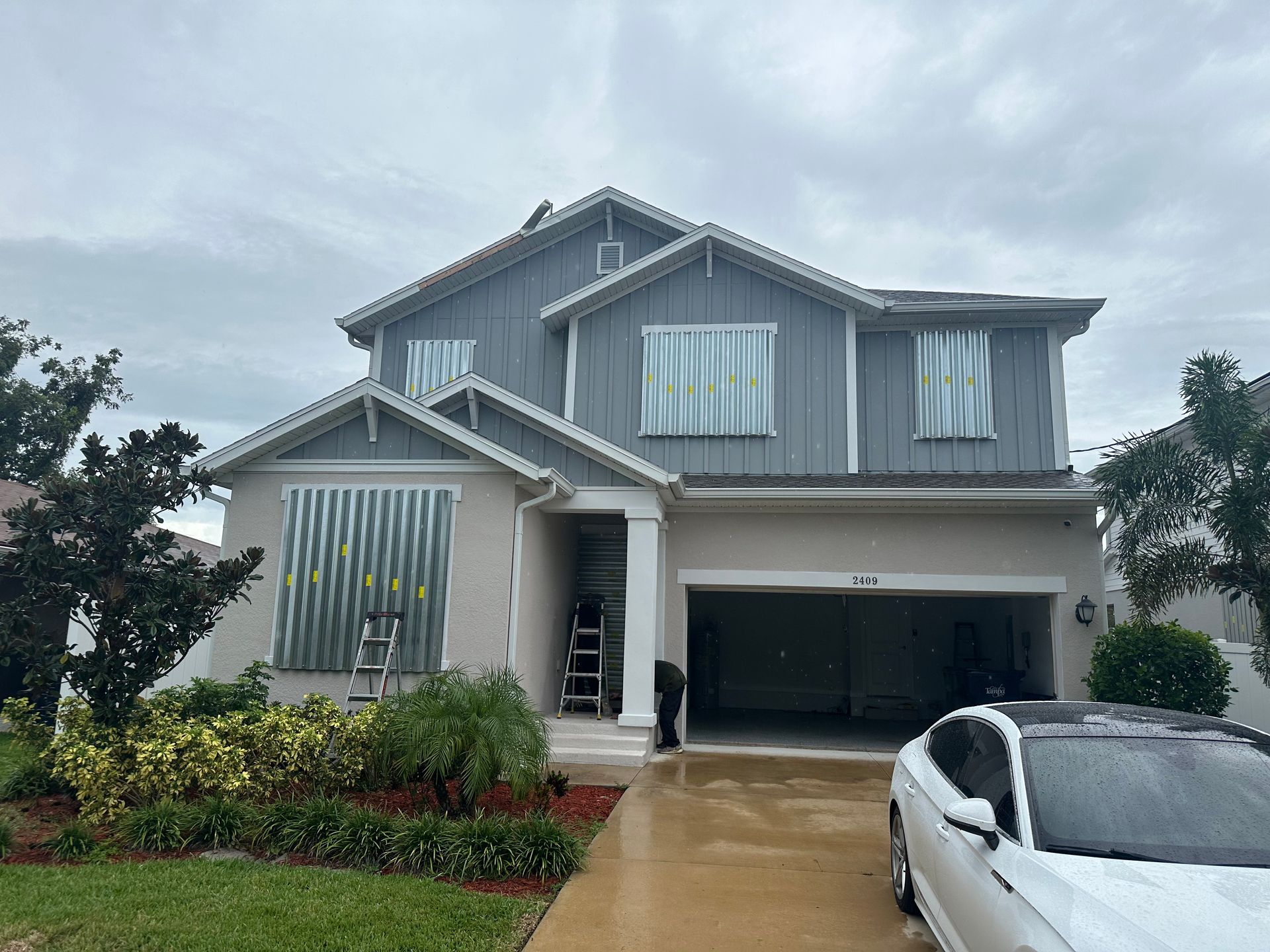 A white car is parked in front of a large house.