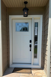 A white front door with a small window and a tall, narrow side light, featuring black hardware and an outdoor light fixture.