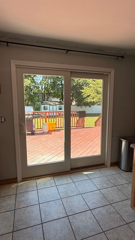 A sliding glass door viewed from inside a room with tiled floors, opening onto a wooden deck overlooking a grassy yard.