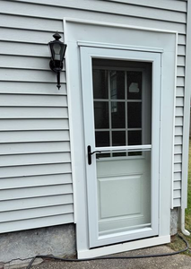 A white storm door with a window and a black handle installed on a house with light gray horizontal siding.