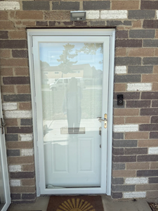 White storm door with a large glass panel and a metal handle, mounted on a brick exterior wall with a doorbell nearby.