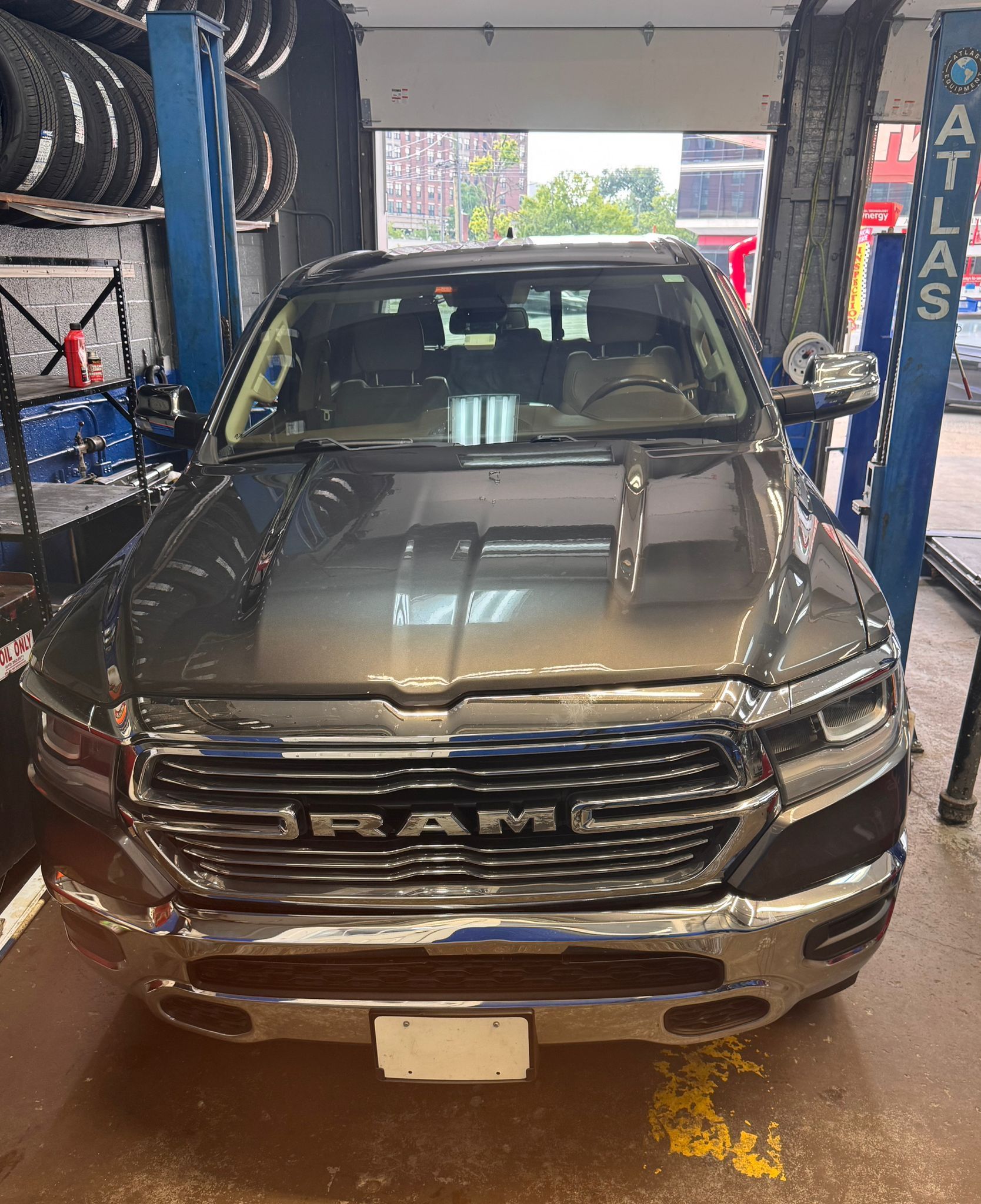 A dark gray Ram pickup truck parked inside a vehicle service bay between two blue hydraulic lifts. | Superior Auto Repair and Tires