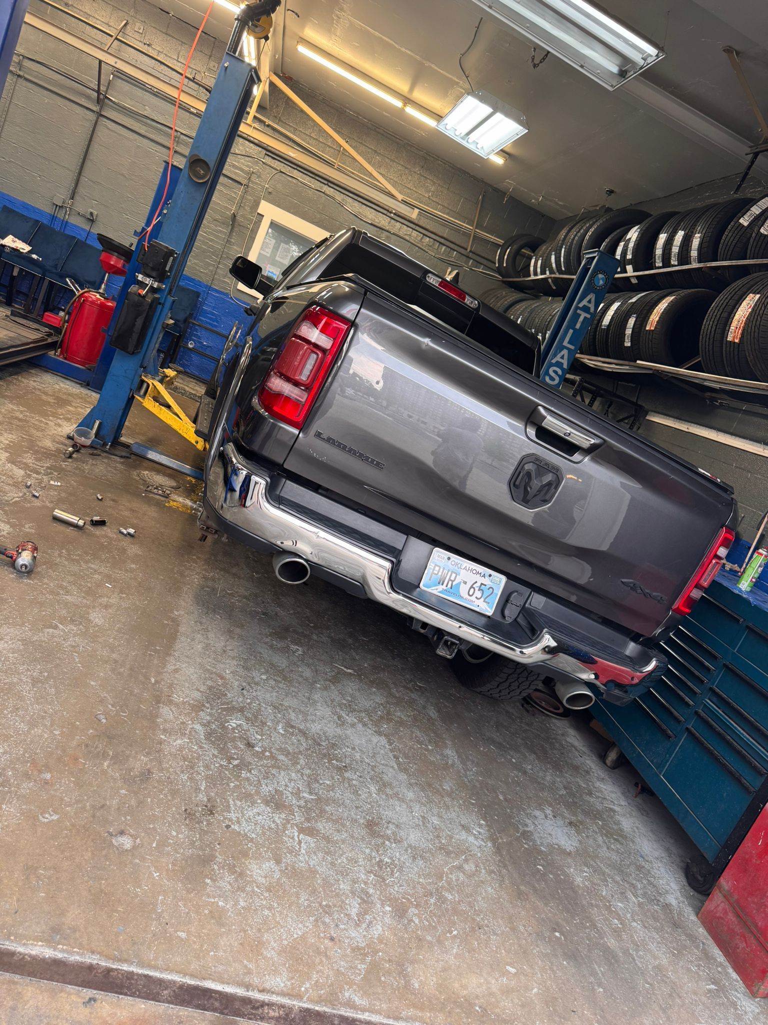 A dark gray Ram truck parked on a vehicle lift inside an auto repair shop with shelves of tires in the background. | Superior Auto Repair and Tires
