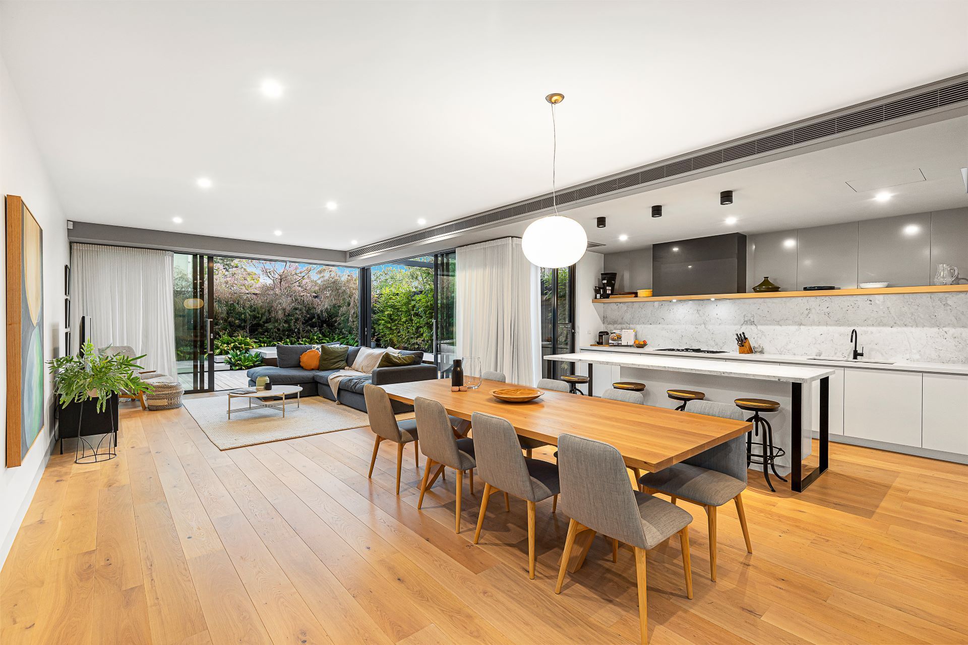 Open-plan kitchen/living area with wood floors, dining table, sofa, and large glass doors leading to an outdoor patio.