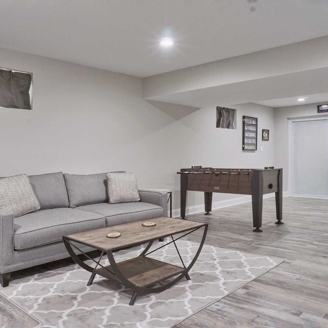 Home theater with large screen, gray sectional sofa, projector, wood paneling, and flooring.