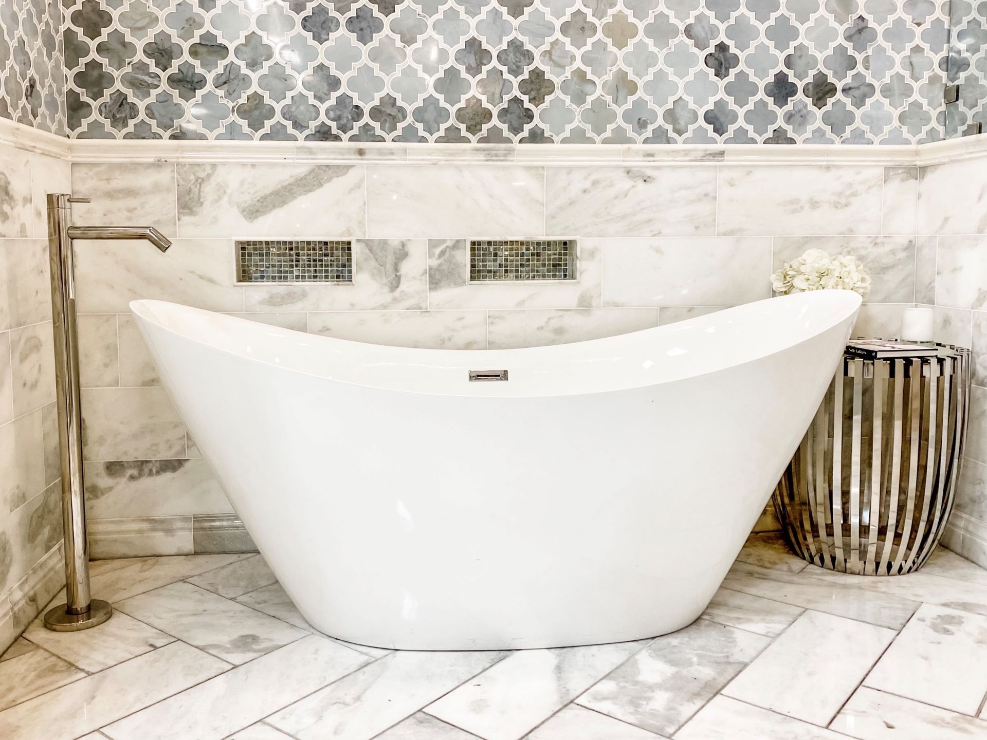 White bathtub in a bathroom with marble tile and a patterned backsplash.