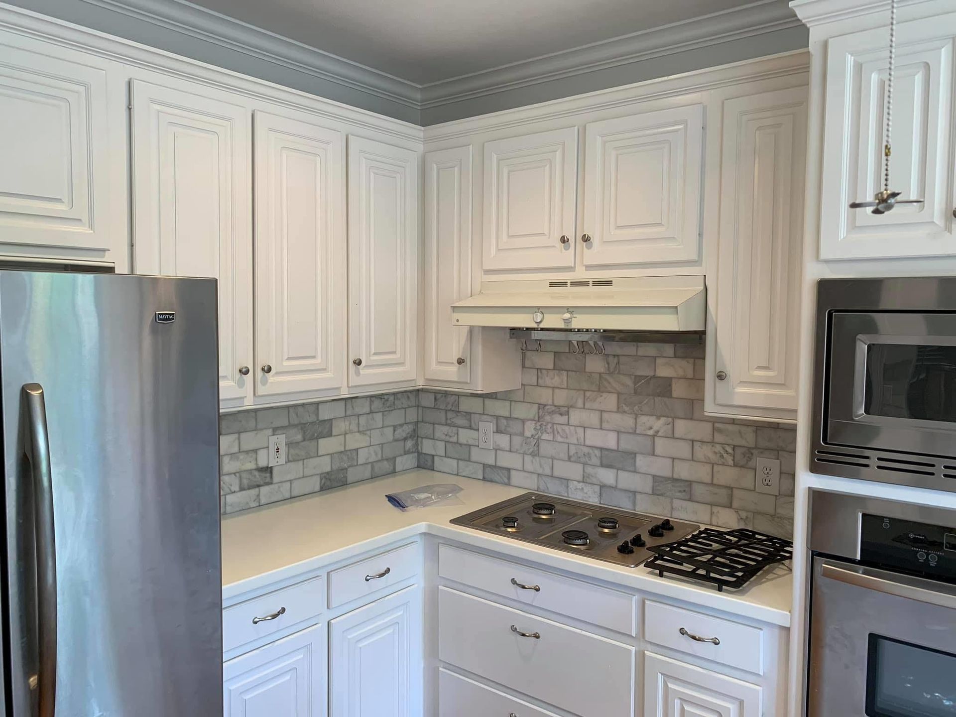 White kitchen cabinets with stainless steel appliances and a grey and white backsplash.