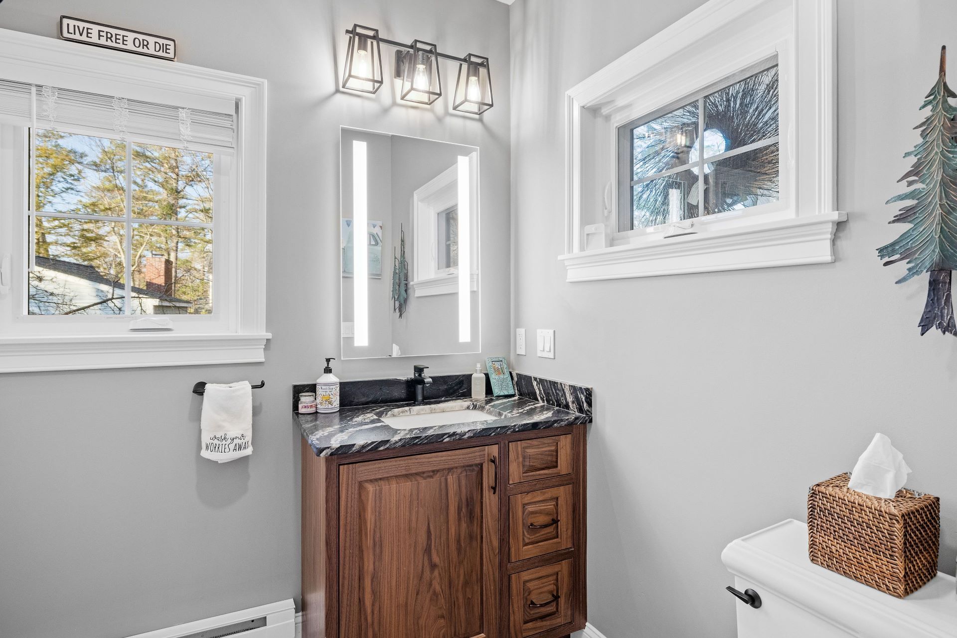 Bathroom with wood vanity, dark countertop, gray walls, and two windows.
