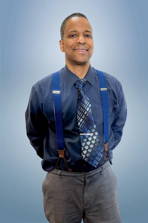 A man in a suit and tie is sitting in front of a window.