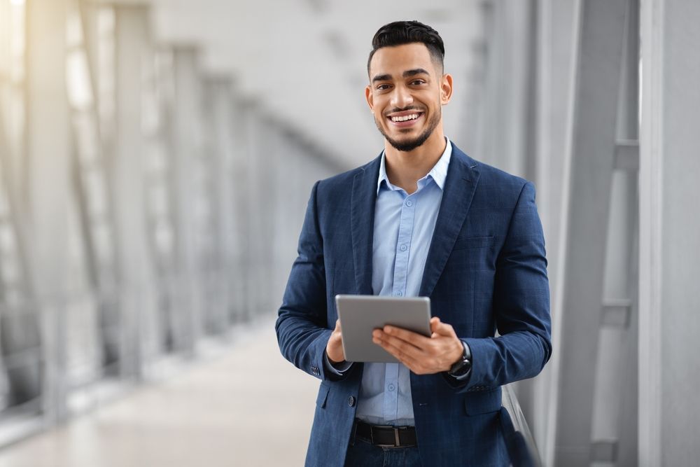 A man in a suit is holding a tablet and smiling.