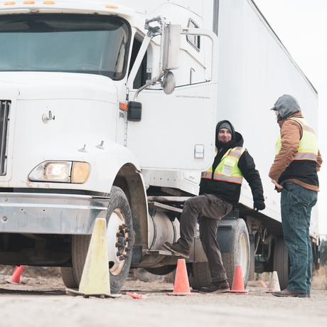 A man is sitting on the back of a semi truck.